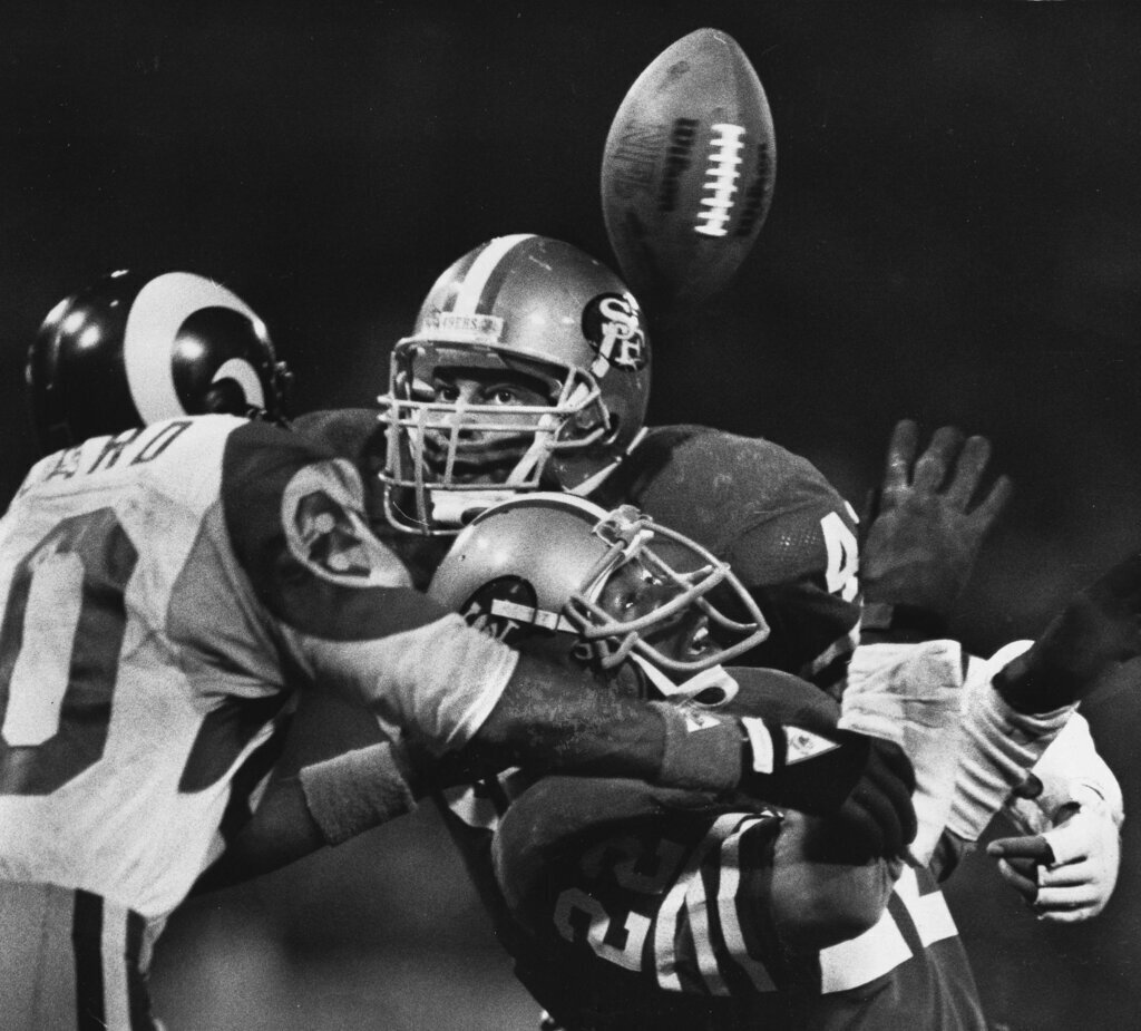 Black-and-white action photo of a quarterback being hit as he releases the football during an NFL game