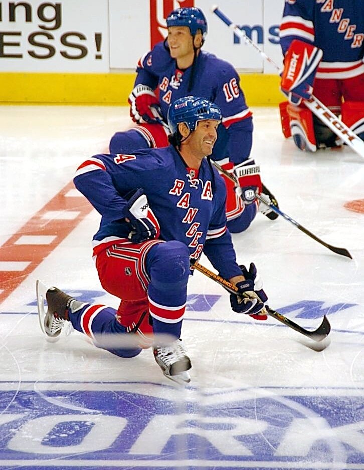 New York Rangers players stretching on the ice during warm-ups, with Mark Messier kneeling in the foreground holding his hockey stick