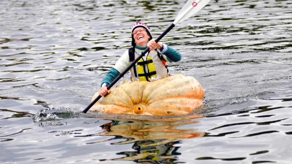 Person kayaking in a giant hollowed pumpkin on a lake during a pumpkin regatta.