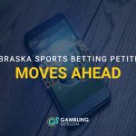 Smartphone on a wooden surface with overlaid text reading “Nebraska Sports Betting Petition Moves Ahead” and the GamblingSites.com logo.