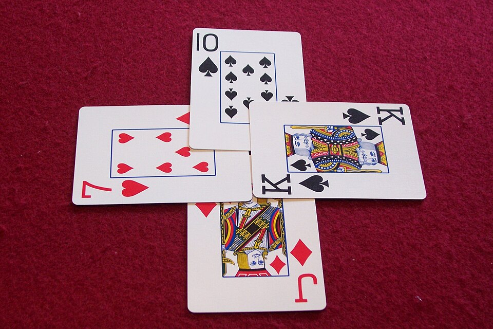 Four playing cards arranged in a cross on a red felt table.