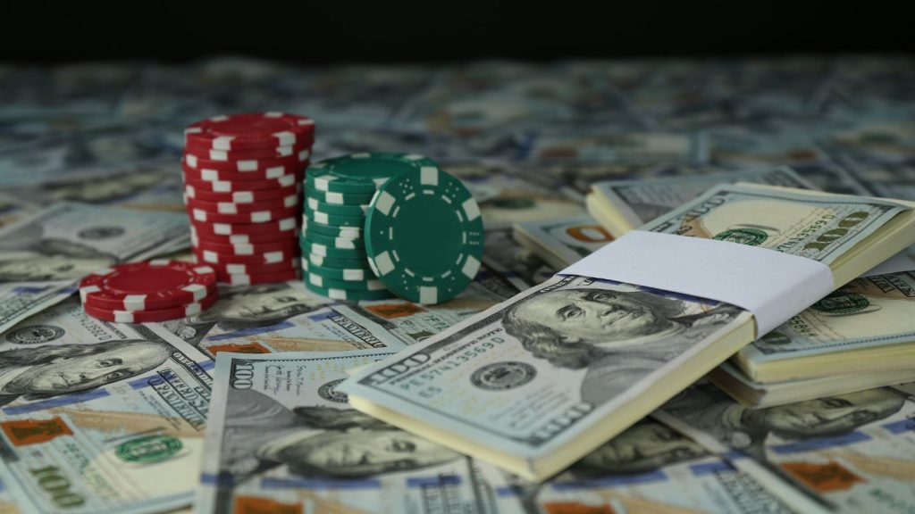 Stacks of red and green casino chips beside bundles of $100 bills scattered across a table.