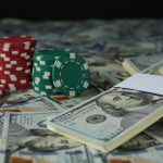 Stacks of red and green casino chips beside bundles of $100 bills scattered across a table.